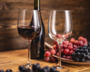 Bottle of dry red wine with a glass and a bunch of grapes on a wooden table. Concept of viticulture and winemaking