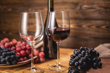 Bottle of dry red wine with a glass and a bunch of grapes on a wooden table. Concept of viticulture and winemaking