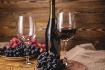 Bottle of dry red wine with a glass and a bunch of grapes on a wooden table. Concept of viticulture and winemaking