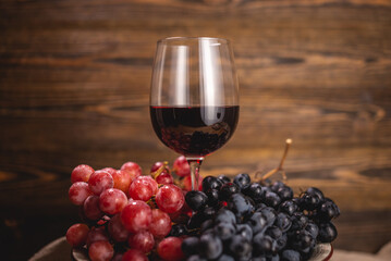 Bottle of dry red wine with a glass and a bunch of grapes on a wooden table. Concept of viticulture...