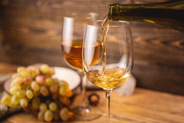 Bottle of dry white wine with a glass and a bunch of grapes on a wooden table. Concept of viticulture and winemaking