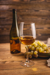 Bottle of dry white wine with a glass and a bunch of grapes on a wooden table. Concept of viticulture and winemaking