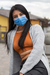 Young Latin woman with long hair wearing a mask, sitting, wearing an orange top and jeans, close up