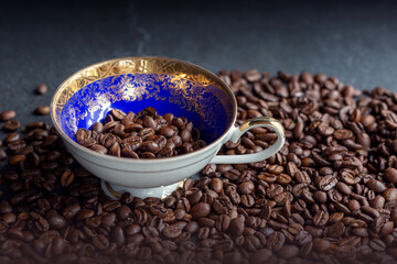 Geröstete Kaffeebohnen in einer Sammeltasse. Kaffeebohnen liegen auf grauem Stein.
