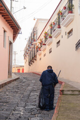 Obraz na płótnie Canvas Man doing cleaning of cobbled street of colonial city - man picking up garbage with a bag and broom in street of the historic center of Quetzaltenango Guatemala