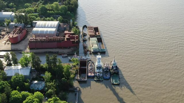 Video desde un dron a lo largo de un ancho r&iacute;o con astillero y muelle a la izquierda y barcos amarrados y barcos hundidos en la costa. 