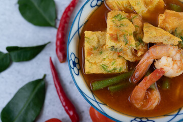 Hot and sour soup with cha-om, egg, and shrimp in a white bowl.