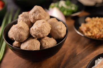 Pork balls in black cups are placed on a wooden table.