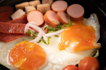 Breakfast with fried eggs, sausage, and ham in a pan with tomatoes. Chili and basil.