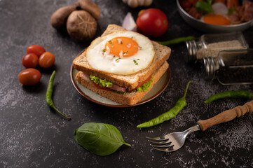 Breakfast sandwich made with bread, fried egg, ham, and lettuce.
