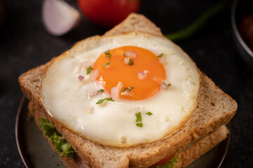 Breakfast sandwich made with bread, fried egg, ham, and lettuce.