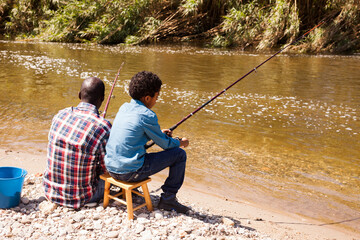 Back portrait of little boy and his father fishing with rods on river