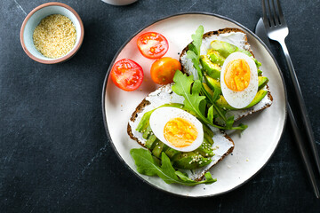 Avocado toasts with cottage cheese, eggs, arugula on darl table. Healthy breakfast, snack. Top view
