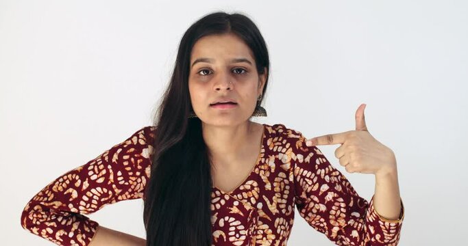 Asian female with black hair points a finger at herself in shock and pleasantly surprised at the result wins victory someone calls her draws attention disbelief good news taken aback smiling concerned