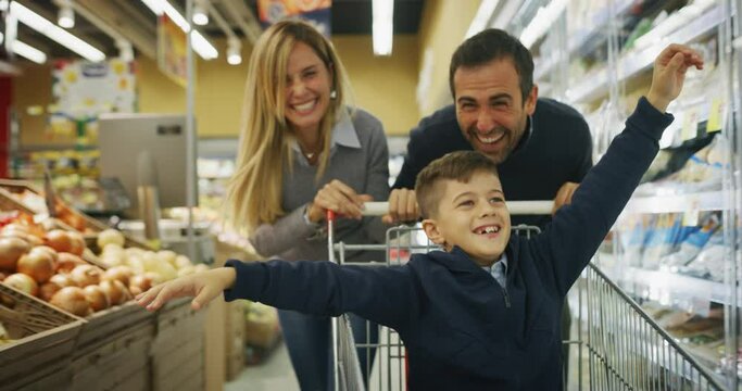 Authentic shot of happy family of father, mother and son are having fun with shopping cart while going for groceries together in supermarket.