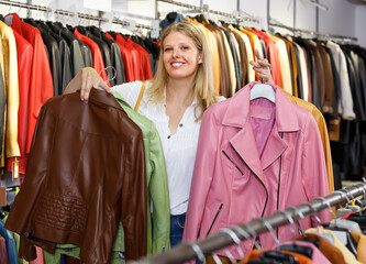 Fototapeta premium Portrait of cheerful woman customer with leather jackets in clothes store