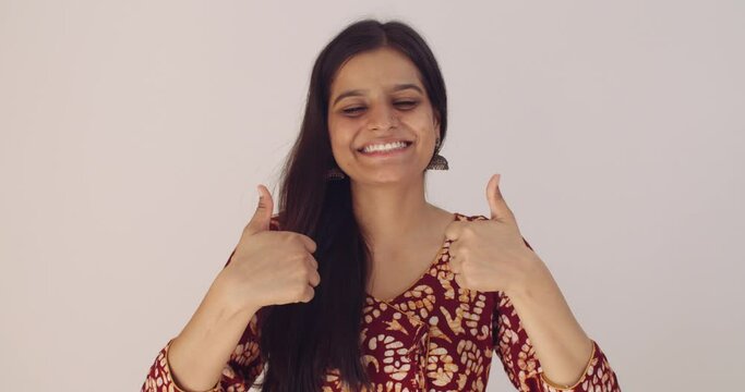 Asian female with black hair hand gestures of best of luck with thumbs raised in shock and pleasantly surprised at the result wins someone calls her draws attention disbelief good news taken aback 