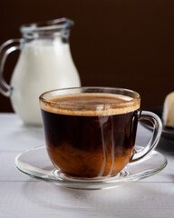 A cup of hot american black coffee with cream poured over. Tasty breackfast with creamy Camembert cheese on natural white wooden table.