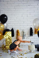 Cute blonde boy on his first birthday at a decorated party in gold, black and silver colors. Baby and first cake. Сrashсake