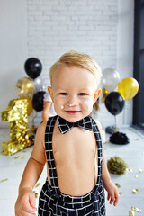 Cute blonde boy on his first birthday at a decorated party in gold, black and silver colors. Soiled in the cake.