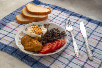Healthy simple breakfast with poached egg, chicken steak, seaweed salad and tomato. Servings on a concrete background with a sealed napkin