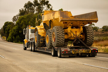 A very large haul dump truck being hauled by an 18 wheel truck down a freeway