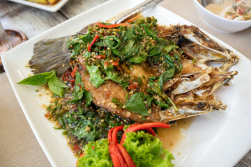 Stir Fried Spicy Fish on a white plate garnished with chili and astringent leaves. Decorate the dish with beautiful vegetables, popular Thai seafood.