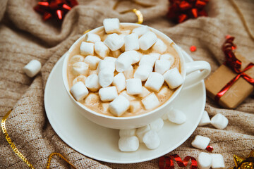 Coffee with marshmallows on a background of knitted fabric with gifts and holiday bows.Hot winter drink.