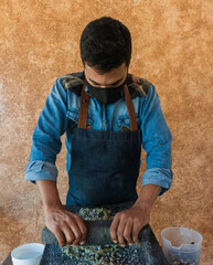 chef grinding corn in stone metate, traditional method to make tortillas, artisan method of...