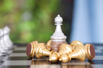 The silver chess pawn standing on a stack of coins and the golden pawn pawns around begging for...