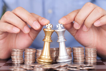 Two hands next to the dollar coin help the two chess kings duel