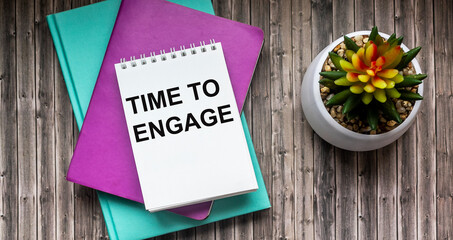 Time to engage , text on white notepad. Colored notepads and a cactus lie on a wooden table.