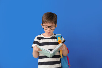 Surprised little schoolboy with book on color background
