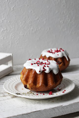 Rum baba poured with white icing on a plate on a table covered with a white tablecloth.