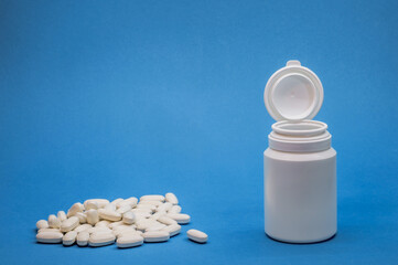 An open white bottle with a pile of scattered pills on a blue background.