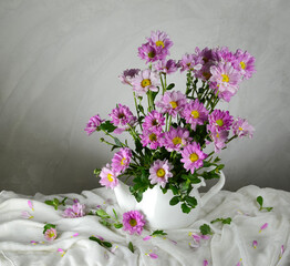 Blooming flowers in a vase, placed on a white cloth, on a vintage wooden table, rough polished cement wall, still life style, beautiful and classic.