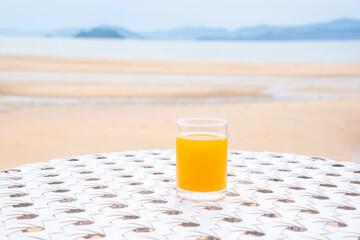 A glass of orange juice on white table next to the beach