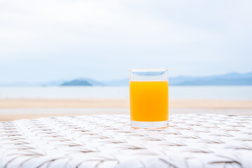 A glass of orange juice on white table next to the beach