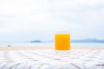 A glass of orange juice on white table next to the beach