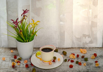 Hot coffee, flowers in a vase and dried flowers placed on a table, with windows lighted by white lace curtains.