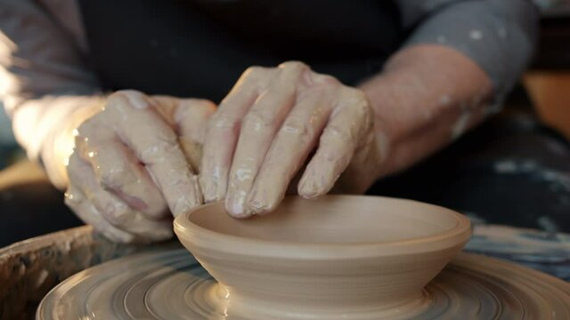 Close-up of potter's hands making bowl from clay using throwing-wheel in workshop busy with handicraft. Creative people and craftsmanship concept.