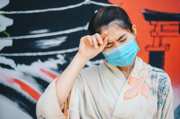 Asian woman in Yukata dress having illness and headache while wearing surgical mask for protect...