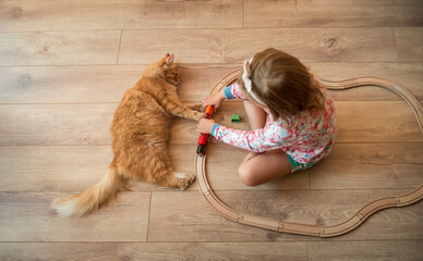 Portrait of cute happy caucasian kid girl and red kitten. Little positive kid sitting and playing...