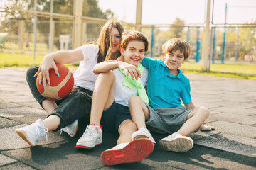 Cheerful high school students sit on the basketball court, relax after the game, talk and laugh. Sports, games, and education. The concept of friendship