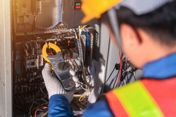 Digital clamp meter in hands of electrician close-up against background of electrical wires and...