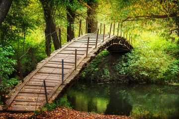 Wooden bridge accross the river. Rustic walkway with autumn leaves. Sunny day