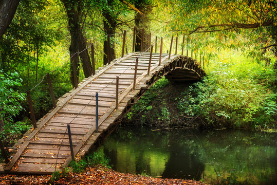 Wooden bridge accross the river. Rustic walkway with autumn leaves. Sunny day - Powered by Adobe