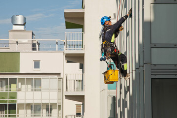 Industrial mountaineering worker hangs over residential building while washing exterior facade glazing. Rope access laborer hangs on wall of house. Concept of urban works. Copy space