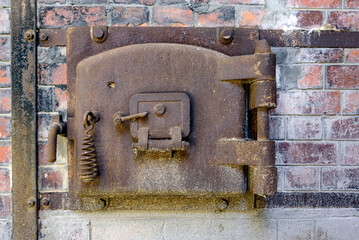 Rusty old metal hatch door of a red brick kiln in an abandoned factory. Rusty metal hatch door with metal frame bolted to old red brick wall.