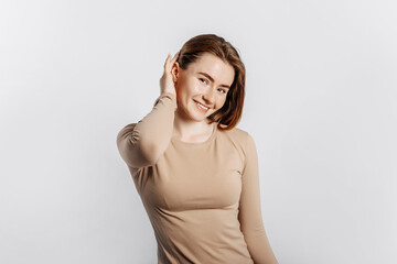 Fototapeta premium Beautiful young girl smiling and posing looking at the camera on a white isolated background. Positive brunette woman in a beige jumper. Kind look.